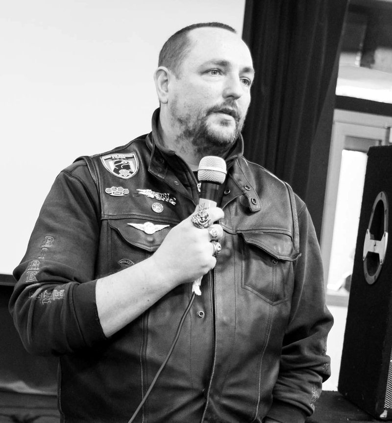 Christophe Arconnerie Bériol, président de THE DEFENDERS, micro à la main, portant son gilet de cuir patché, lors d’une prise de parole.